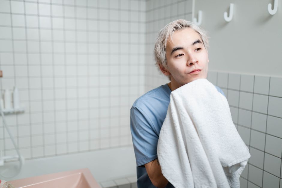 洗面所でタオルで顔を押さえている男性